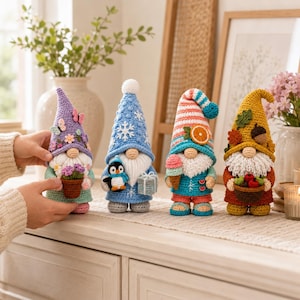 May include: Four crocheted gnome figurines representing different seasons. The first is purple with flowers, the second is blue with a penguin and gift, the third is striped with an orange slice and ice cream, and the fourth is yellow with autumn leaves and a basket of apples.