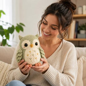 May include: A crocheted owl plush toy featuring a sage green body, a cream-colored belly with small embroidered star details, large dark brown eyes, a small yellow beak, and orange feet. The owl has textured wings and small ear tufts.