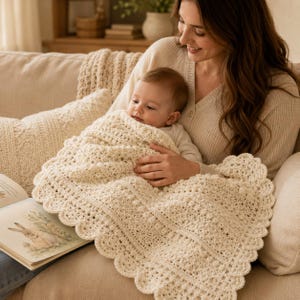 May include: A cream-colored, hand-crocheted baby blanket featuring a textured bobble stitch pattern and a decorative scalloped edge. The blanket is rectangular with a dense, intricate knit design, providing a soft and uniform appearance.