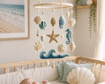 May include: A hanging nursery mobile featuring crocheted ocean-themed elements including a starfish, seahorse, seashells, coral, and a blue wave. The items are suspended from a circular frame with wooden beads and white string in a neutral color palette.