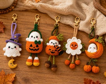 May include: Five handmade crochet keychains featuring Halloween themes: a ghost in a purple witch hat with a yellow moon, a ghost in a pumpkin bucket, a ghost in a pumpkin with a scarf, a white flower with orange berries, and a ghost on a crescent moon.