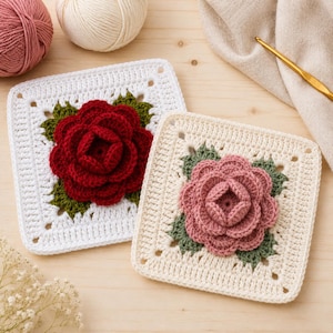 May include: Two square crochet motifs featuring three-dimensional flowers. One motif has a white border with a deep red rose and green leaves. The other has a cream border with a dusty pink rose and green leaves. Both are made of yarn.