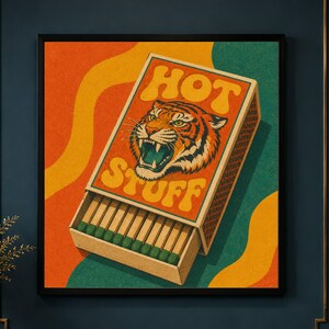May include: A square wall art print featuring a matchbox illustration with a tiger head graphic and the text HOT STUFF. The design uses a colour palette of orange, yellow, and green with a textured finish, showing matches inside the box.