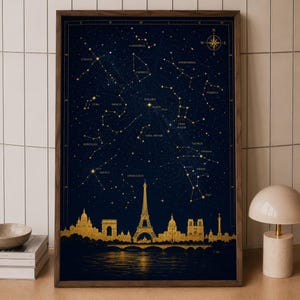 May include: A framed vertical wall art print featuring a dark navy blue night sky filled with gold constellations and a compass rose. Below the stars, a gold silhouette of the Paris skyline, including the Eiffel Tower, reflects on water.