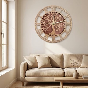 Puede incluir: Un reloj de pared circular con un marco de madera de color claro y números romanos. El centro muestra una silueta de árbol de madera cortada con láser sobre un fondo circular marrón oscuro, con manecillas finas de color claro.