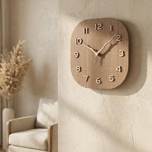 Può includere: Un orologio da parete quadrato in legno con angoli arrotondati, caratterizzato da una finitura in venature del legno marrone chiaro. Il quadrante presenta numeri arabi in rilievo marrone scuro da 1 a 12 e due lancette a forma di rami.
