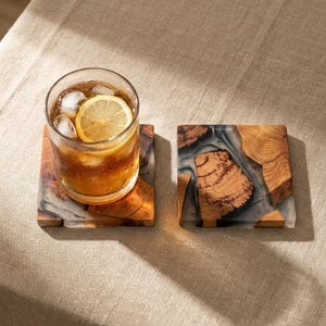 Peut inclure: Deux dessous de verre carrés composés de tranches de bois naturel incrustées dans de la résine grise translucide. L'un des dessous de verre porte un verre transparent rempli d'une boisson ambrée, de glaçons et d'une rondelle de citron.