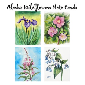 May include: Set of four watercolor note cards featuring Alaskan wildflowers. The cards depict a purple iris, pink wild roses, pink fireweed, and blue bellflowers.