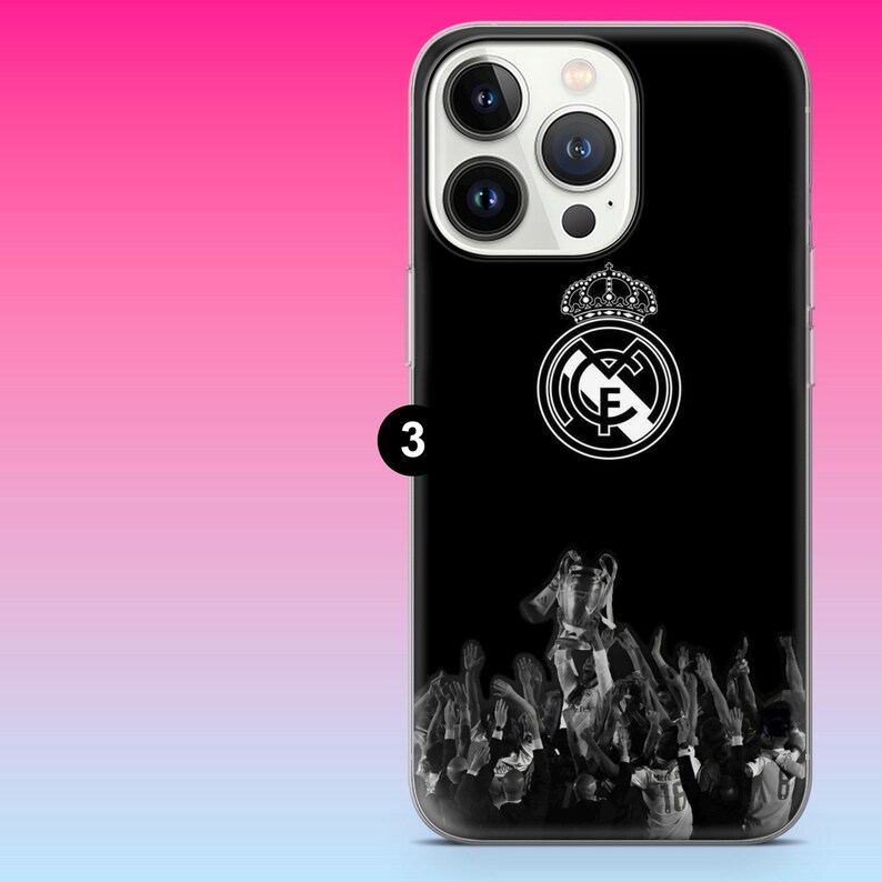 May include: A black smartphone case featuring a white Real Madrid club crest at the top and a monochrome graphic of a crowd lifting a trophy at the bottom. The case has a cutout for a triple-lens camera system and a small black circle with the number 3.