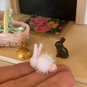 May include: A white fluffy bunny with pink ears and iridescent glitter, and a brown chocolate bunny figurine.