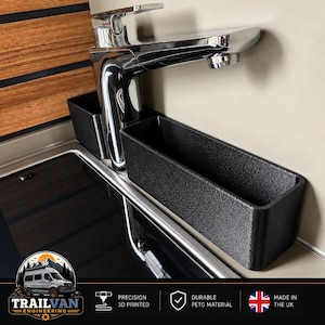 May include: A black rectangular storage caddy with a textured finish, designed to fit around a chrome faucet. The caddy features two separate compartments for organizing small items, positioned directly behind a sink basin in a van interior.