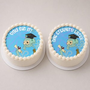Könnte beinhalten: Zwei runde Kuchen mit weißem Zuckergussrand. Der linke Kuchen hat eine blaue Oberfläche mit einer Zeichentrickfigur, die eine Doktorhut trägt und ein Diplom hält, mit dem Text "YOU DID IT!". Der rechte Kuchen trägt den Text "ONE ETERNITY LATER".