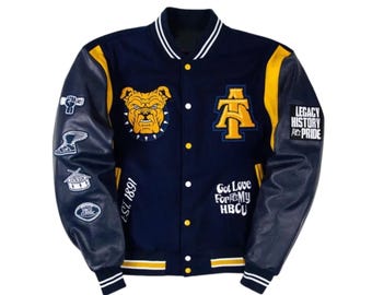Könnte beinhalten: Eine marineblaue Collegejacke mit gelben und weißen Akzenten, einem Bulldoggen-Aufnäher, einem AT-Logo und dem Text EST. 1891, Got Love For My HBCU und LEGACY HISTORY PRIDE. Die dunkelblauen Ärmel sind mit verschiedenen gestickten Aufnähern versehen.
