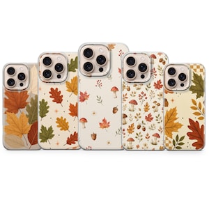 May include: Five smartphone cases arranged in a row, each featuring a cream-colored background with various autumn-themed patterns including orange, red, and green maple leaves, acorns, small mushrooms, and berries, all with a triple camera cutout.