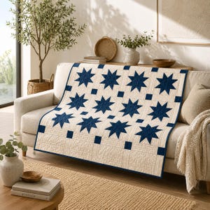 May include: A rectangular quilt featuring a repeating pattern of dark navy blue eight-pointed stars set against a cream-colored background. The design includes small navy blue square accents between the stars and a solid navy blue border edge.