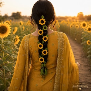 May include: A long, dark braided hairstyle adorned with a series of small, crocheted sunflower hair accessories. Each sunflower features bright yellow petals and a dark brown center, interspersed with small green crocheted leaves and tassels.