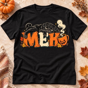 Pode incluir: Uma t-shirt preta com um gráfico de um pug preto deitado sobre o texto laranja e branco "MEH". Ao lado do texto, há uma caneca laranja de abóbora de Halloween com vapor em forma de fantasma, rodeada por folhas de outono espalhadas.
