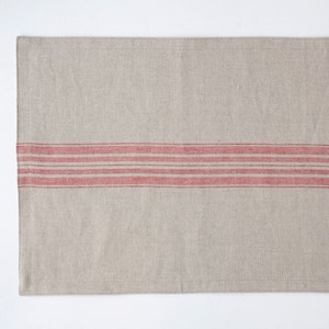 May include: A natural linen placemat with a red stripe design. The placemat is rectangular and has a subtle texture.