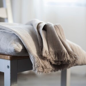 May include: A soft, light brown linen throw blanket with fringe edges draped over a chair.