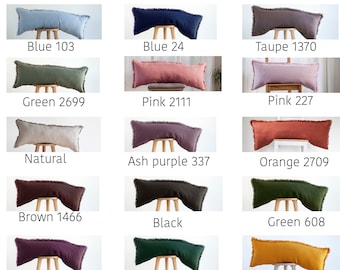 May include: A set of 12 decorative bolster pillows in various colours, including blue, green, pink, natural, ash purple, orange, brown, black, plum, yellow, and taupe. Each pillow has a fringed edge and is made of 100% linen with a hidden zipper closure. The pillows are displayed on wooden stools.