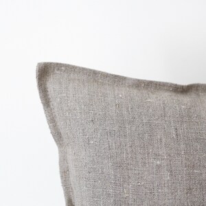 May include: Close-up of a light brown linen pillow cover with a subtle textured weave. The fabric is soft and natural, with a slightly rough feel.