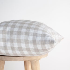 May include: A beige and white gingham pillow resting on a wooden stool. The pillow is made of a soft, textured fabric.