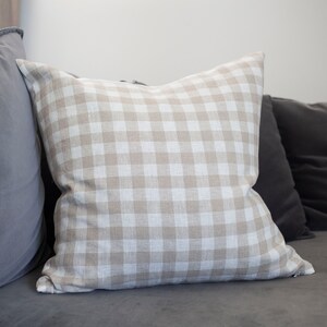 May include: A beige and white gingham throw pillow on a gray couch.