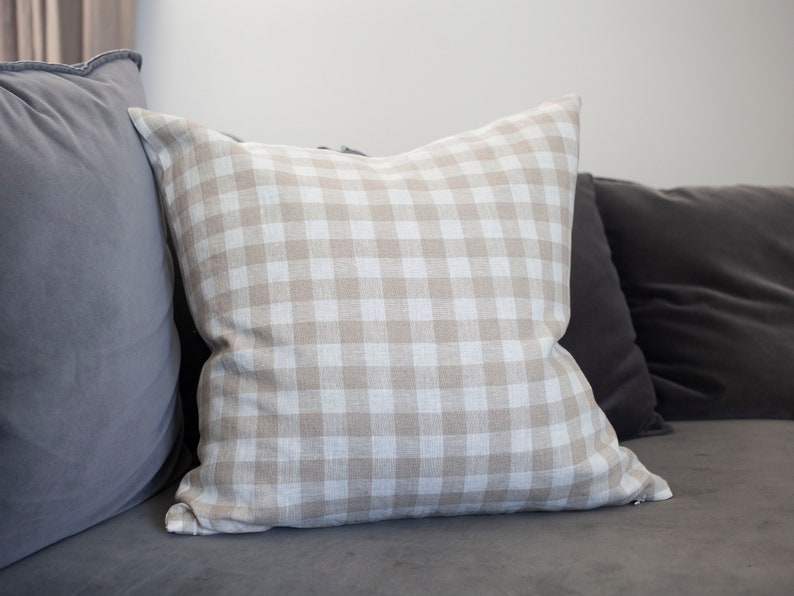 May include: A beige and white gingham throw pillow on a gray couch.