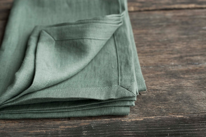 May include: A folded sage green linen napkin on a rustic wooden surface.