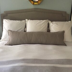 May include: A bed with a gray headboard and white bedding. There are three white pillows and a long brown lumbar pillow on the bed.