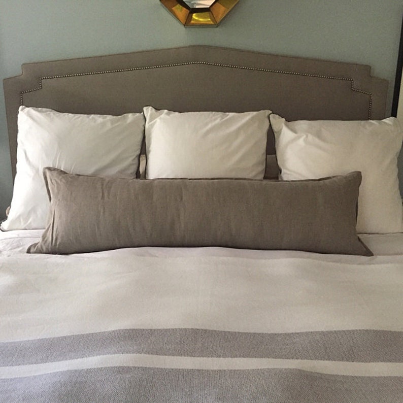 May include: A bed with a gray headboard and white bedding. There are three white pillows and a long brown lumbar pillow on the bed.