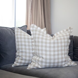 May include: Two beige and white gingham throw pillows with frayed edges on a gray couch.