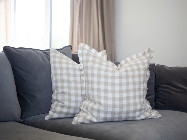 May include: Two beige and white gingham throw pillows with frayed edges on a gray couch.