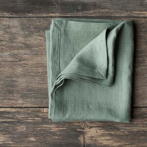 May include: A folded sage green linen napkin on a rustic wooden surface.