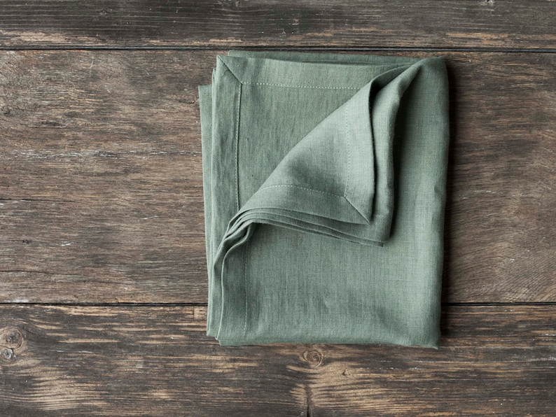 May include: A folded sage green linen napkin on a rustic wooden surface.