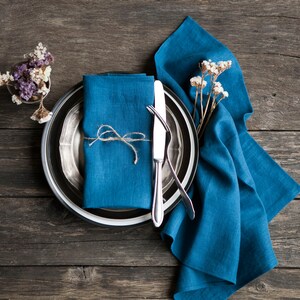 Peut inclure: Une serviette en lin bleu nou&eacute;e avec de la ficelle, plac&eacute;e sur un chargeur argent&eacute; avec un bord noir, et un couteau et une fourchette en argent. Le d&eacute;cor est sur une table en bois rustique.