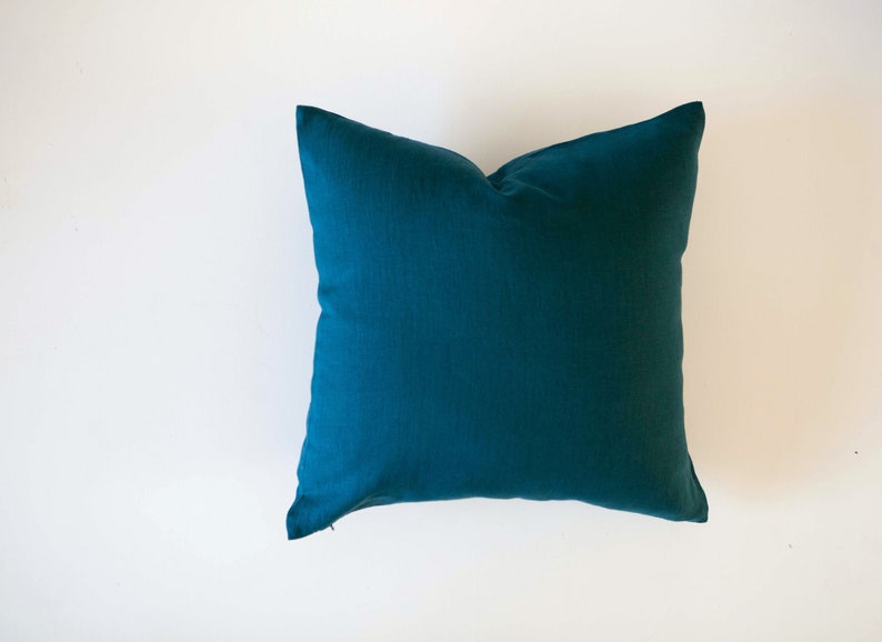May include: A teal blue square cushion with a smooth, solid fabric surface.