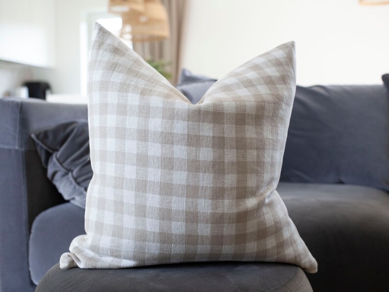 May include: A beige and white gingham throw pillow with a soft, textured fabric. The pillow is sitting on a gray couch.