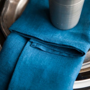 Peut inclure: Une serviette en lin bleu pli&eacute;e sur un plateau en argent. La serviette est pli&eacute;e de mani&egrave;re simple et &eacute;l&eacute;gante, et le tissu a un aspect doux et textur&eacute;.