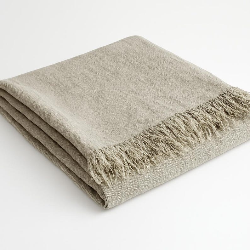 May include: A light brown linen throw blanket with a fringe border.
