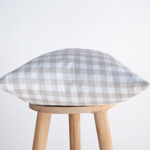 May include: A beige and white gingham pillow sits on a wooden stool. The pillow is made of linen and has a soft, textured feel.
