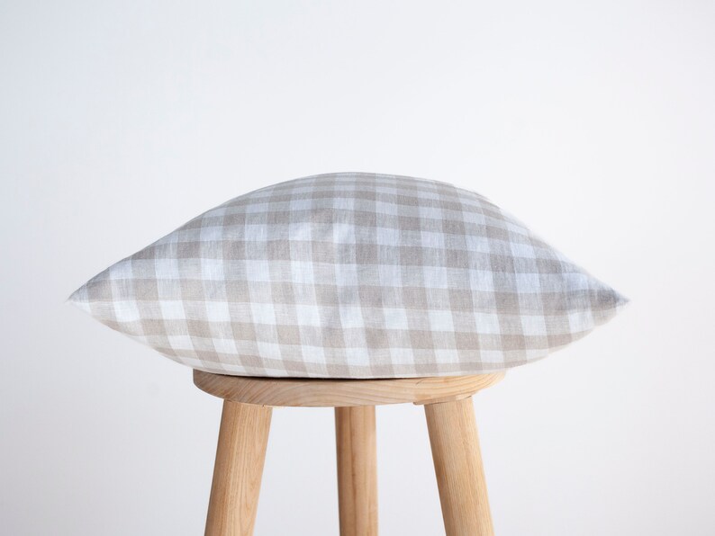 May include: A beige and white gingham pillow sits on a wooden stool. The pillow is made of linen and has a soft, textured feel.