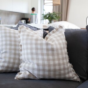 May include: Two beige and white gingham throw pillows with frayed edges on a dark gray couch.
