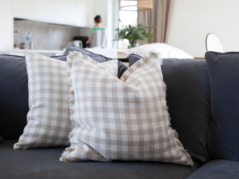 May include: Two beige and white gingham throw pillows with frayed edges on a dark gray couch.