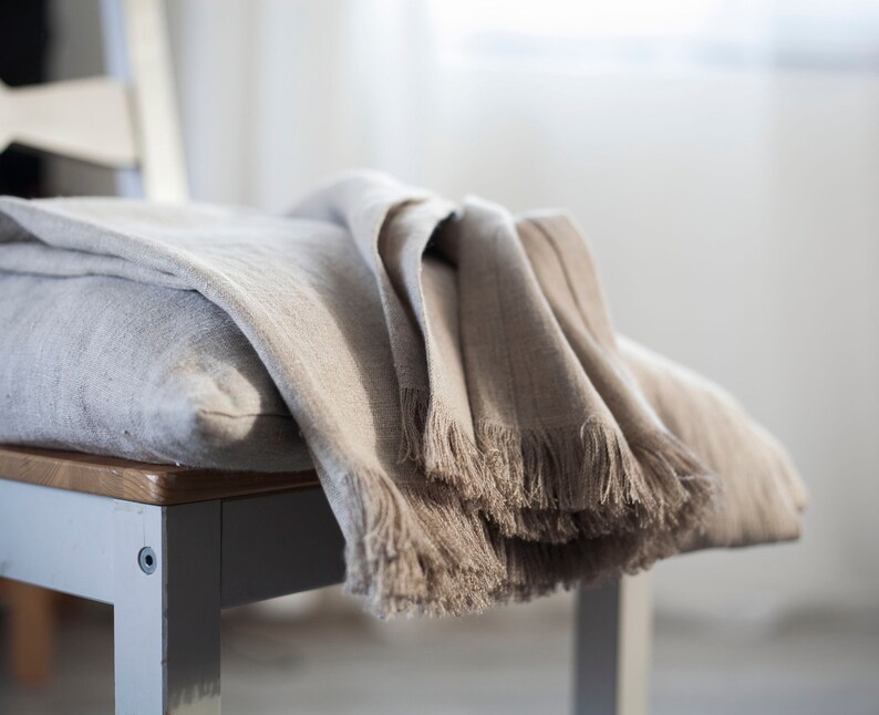 May include: A soft, light brown linen throw blanket with fringe edges draped over a chair.