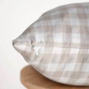 May include: A close-up of a beige and white gingham pillow with a zipper closure.