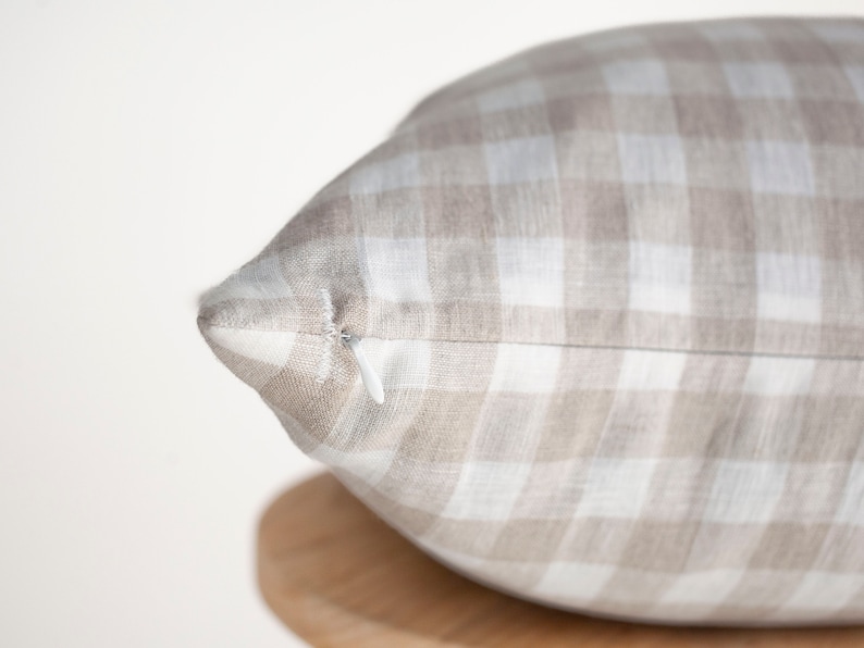 May include: A close-up of a beige and white gingham pillow with a zipper closure.