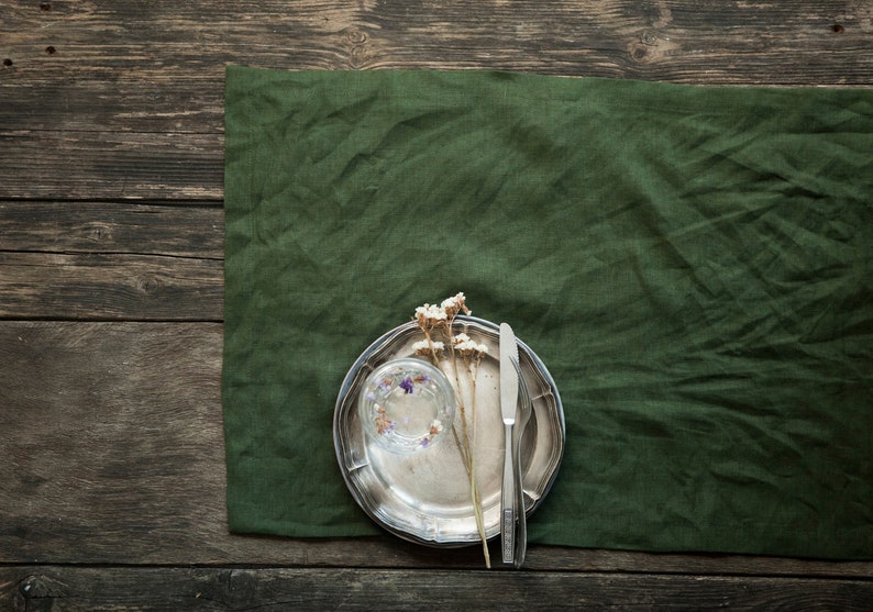 May include: A silver plate with a glass cup and dried flowers on a green linen tablecloth. The plate is on a wooden surface.