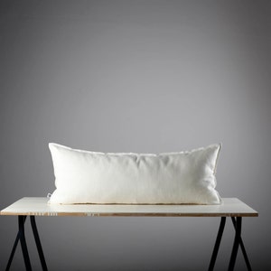May include: A white rectangular pillow resting on a wooden table with black metal legs against a gray background.