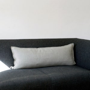 May include: A light gray linen lumbar pillow resting on a dark gray sofa.
